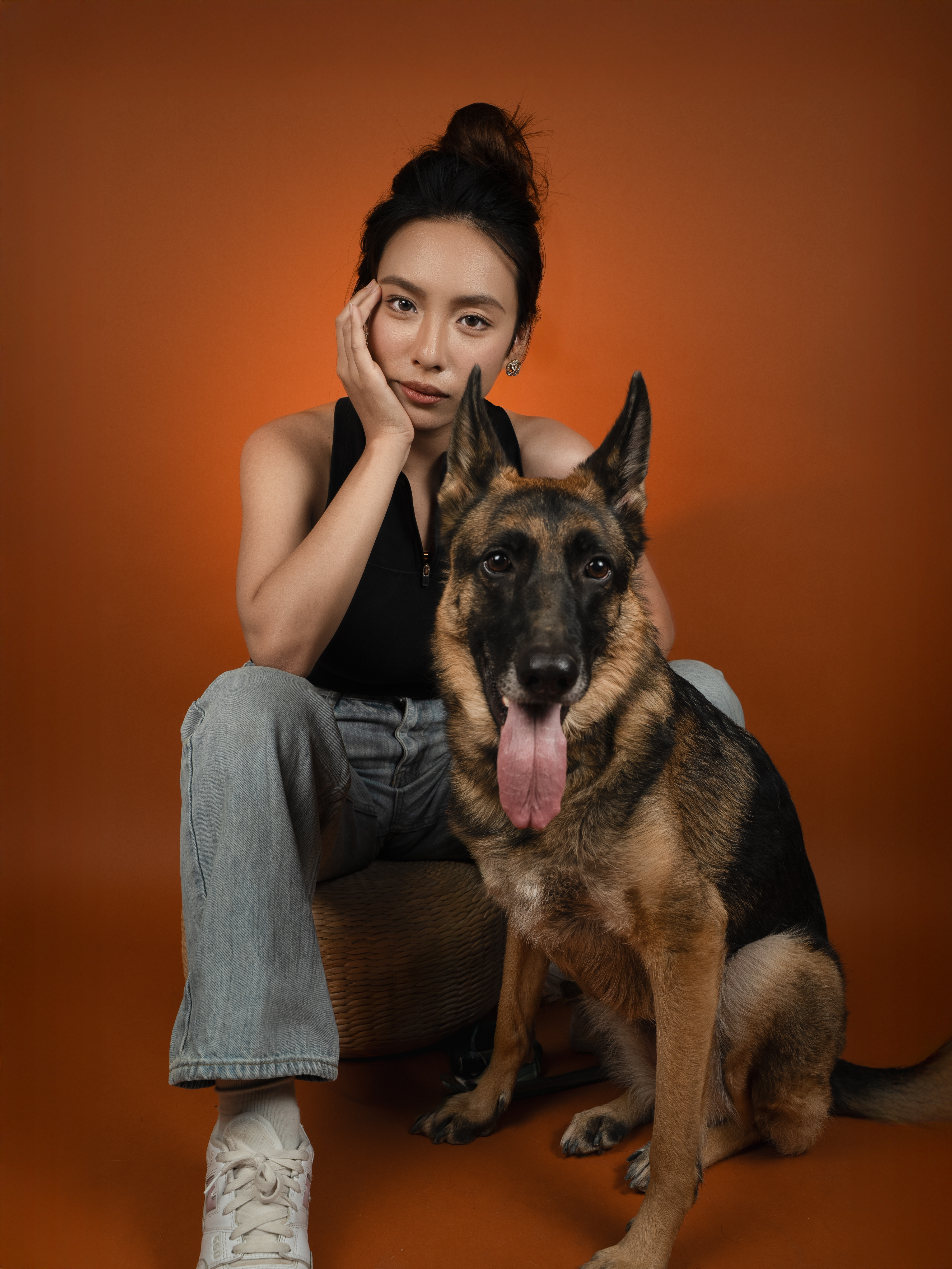 Woman posing with her German shepherd in a studio with warm orange backdrop