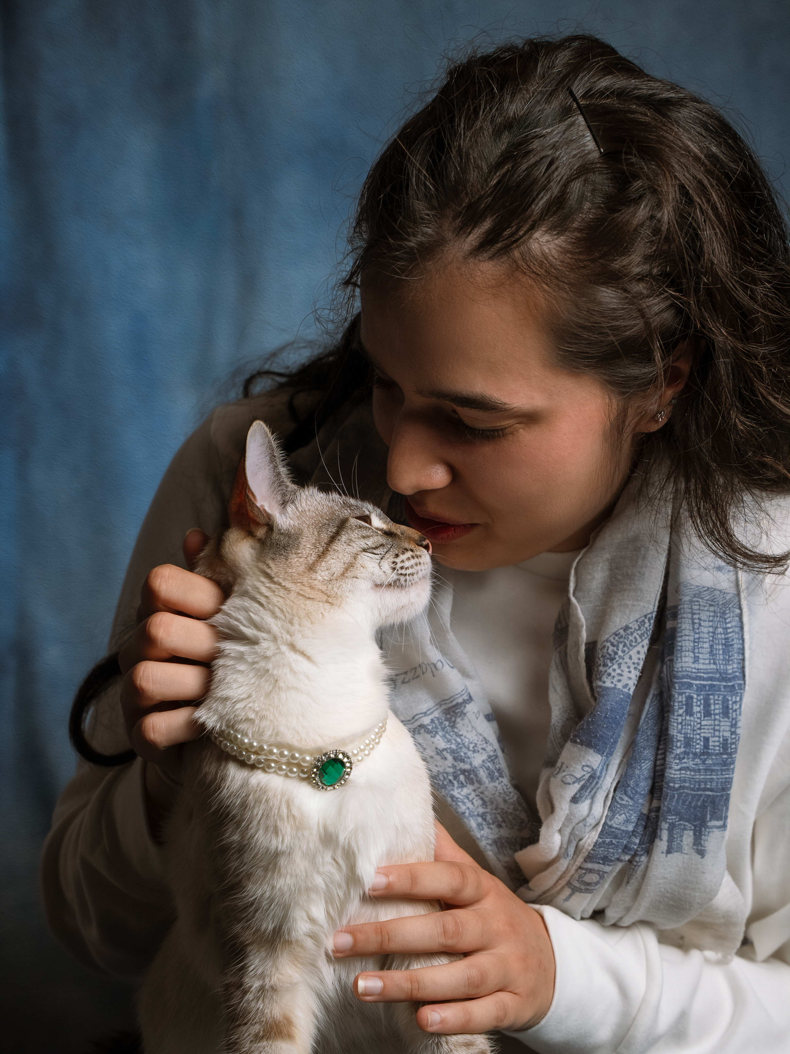 Woman sharing a tender nose-to-nose moment with her cat wearing a pearl necklace